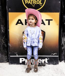 A little girl in jeans, a pink cowboy hat and brown cowboy boots at PBR in Chicago.