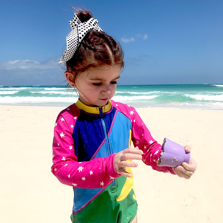 A toddler stands on the beach in Punta Cana wearing a top knot.