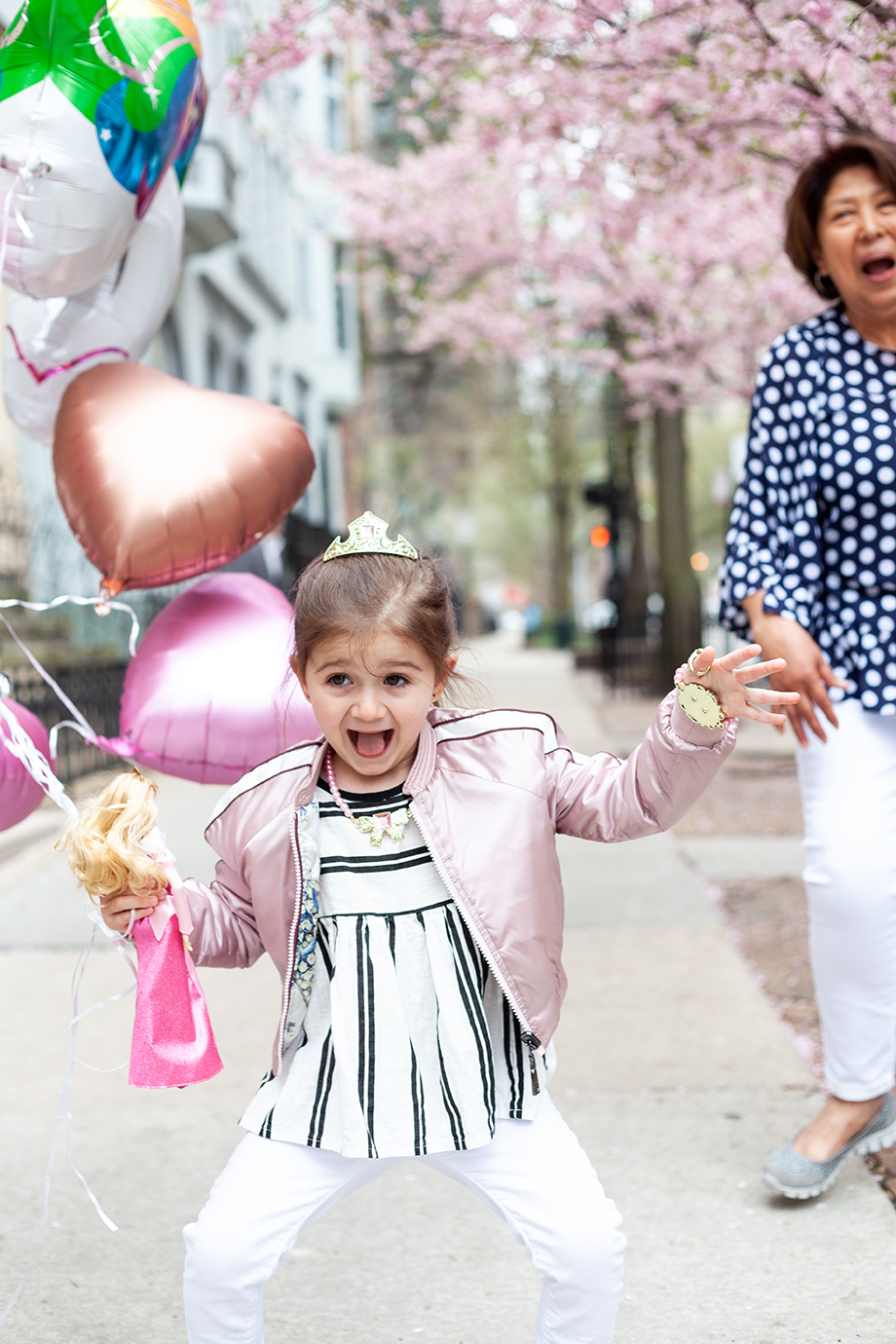 Zelda of Glitter and Bubbles wears a pink jacket and striped shirt while holding balloons. 