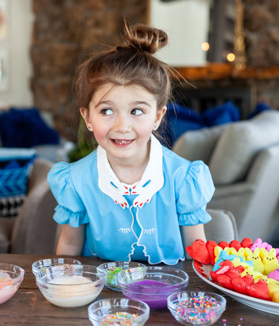 A little girl wears a blue Easter dress while making frosted peeps on Glitter and Bubbles.